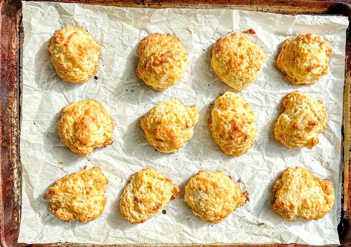 fluffy drop biscuits on a parchment paper lined sheet tray.