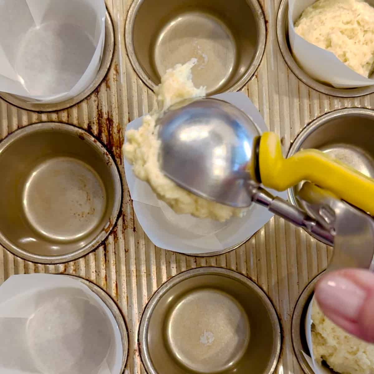 closeup of adding muffin batter to a lined muffin tin.