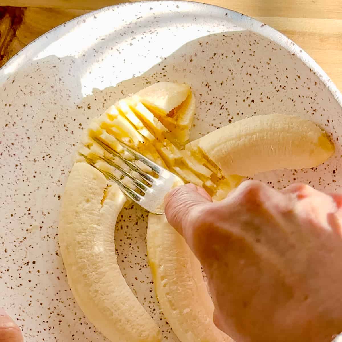 mashing bananas in a white bowl using a fork.