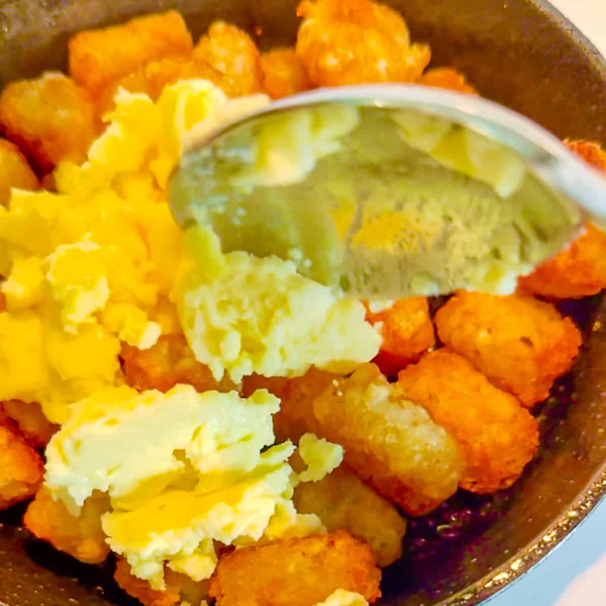 scooping scrambled eggs on top of tater tots.