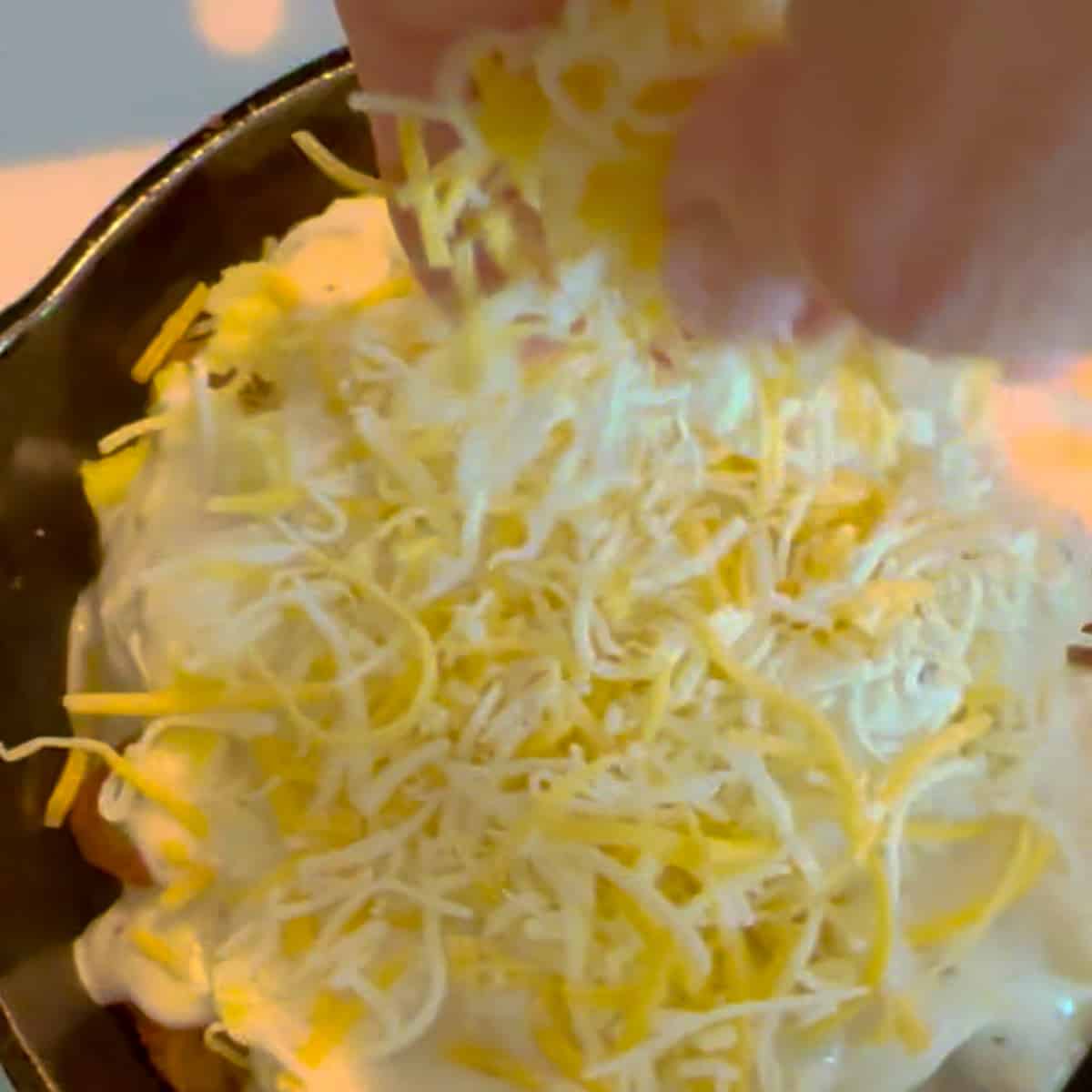 adding shredded cheese to the top of tater tot poutine.
