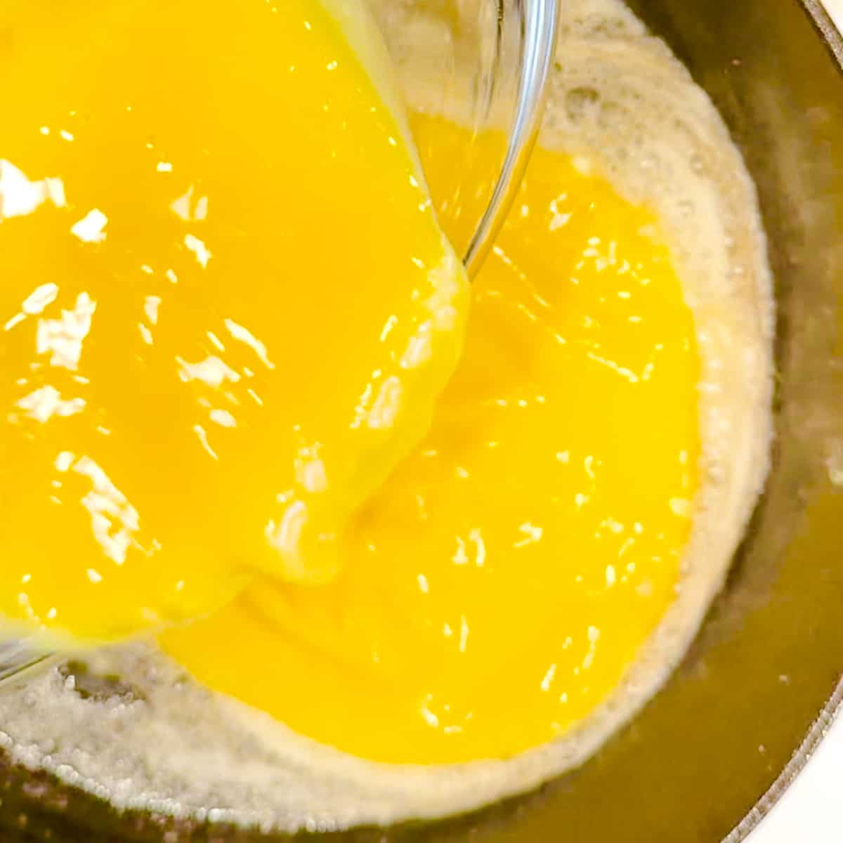 pouring whisked eggs into cast iron skillet.
