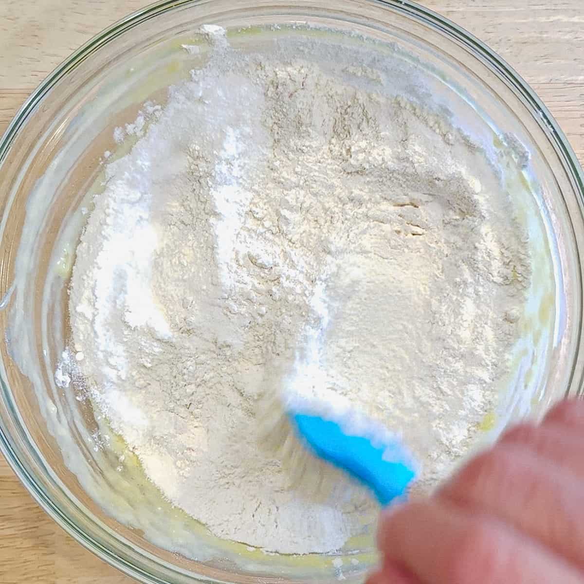 Using a spatula to mix the dry ingredients on top of muffin batter.