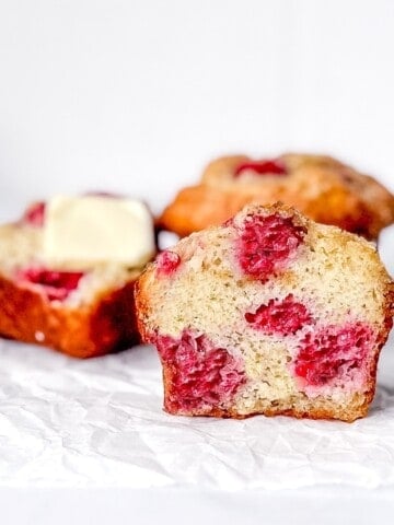 Front view of a sliced raspberry banana muffin with other muffins behind.