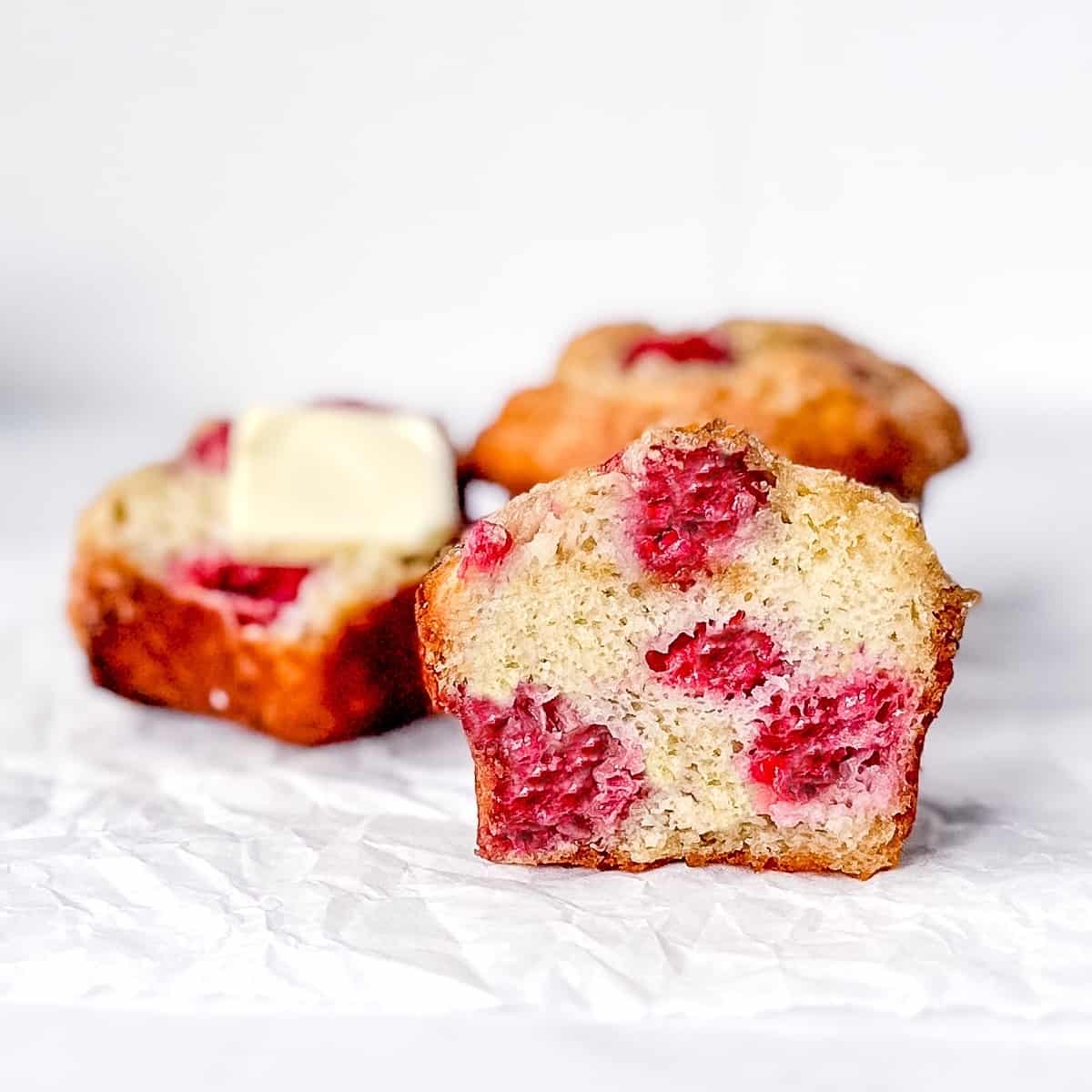 Front view of a sliced raspberry banana muffin with other muffins behind.