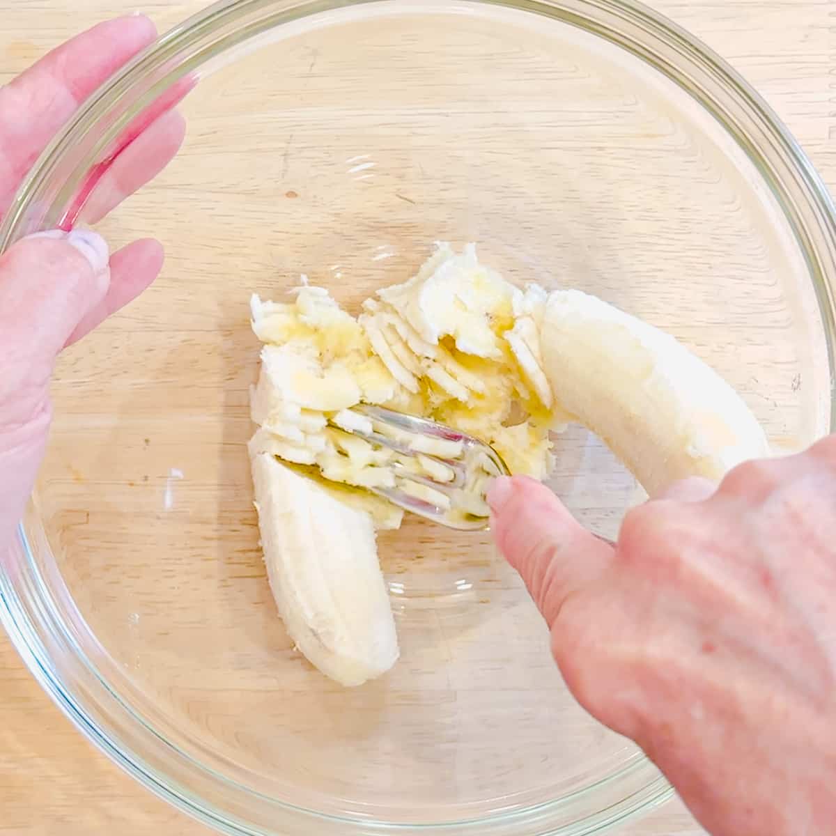 Mashing a banana with a fork in a glass bowl.