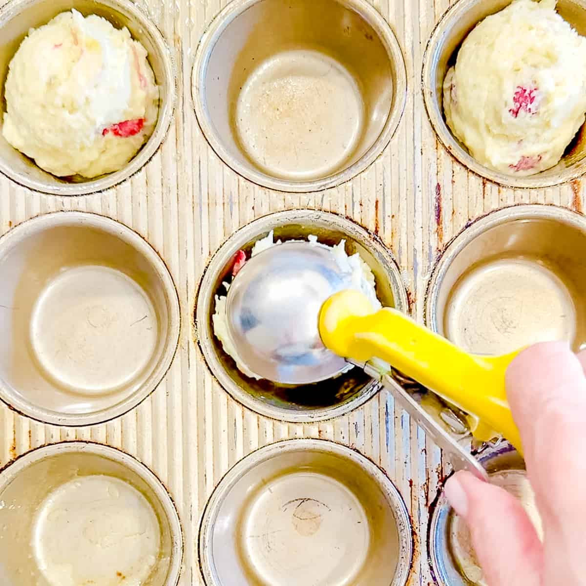 Scooping raspberry banana muffins into a muffin pan.