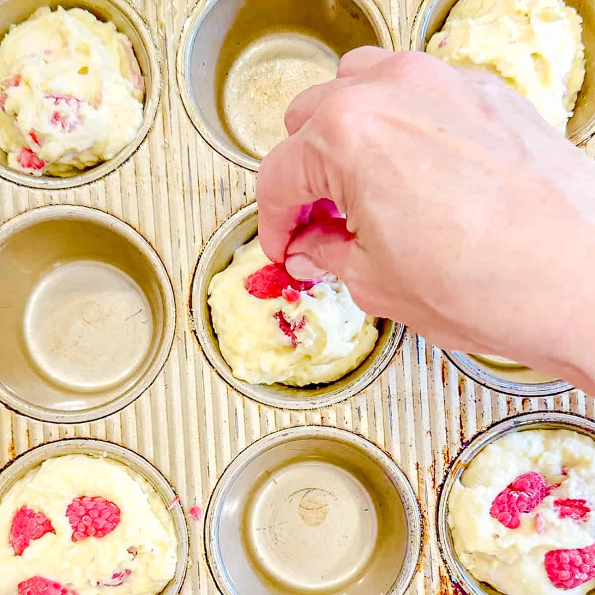 Pressing raspberries on top of unbaked muffins.