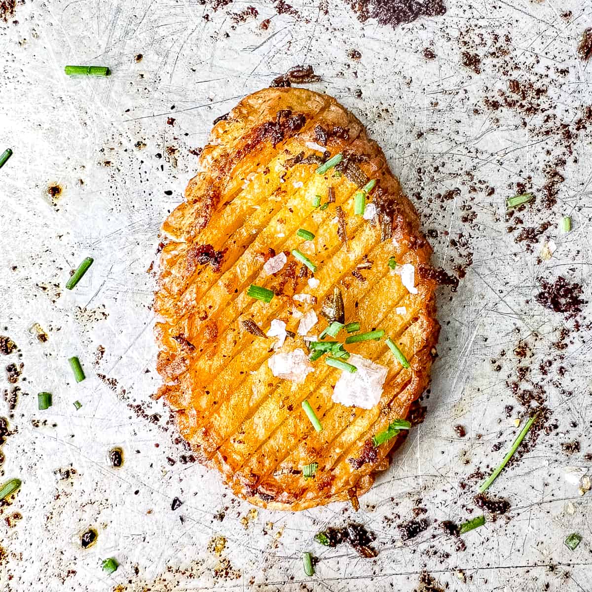 Crispy accordion potato with herbs and flaky salt on a sheet pan.