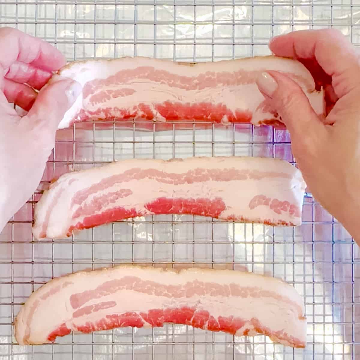 Placing raw bacon strips on a wire rack set on a large sheet pan.