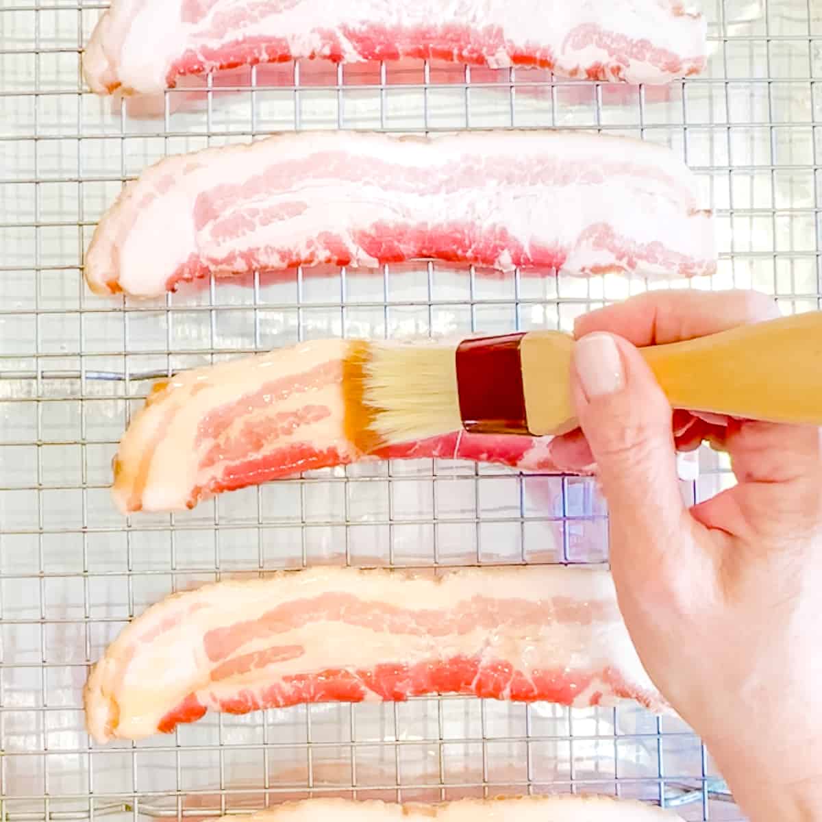 Brushing raw bacon with maple syrup.