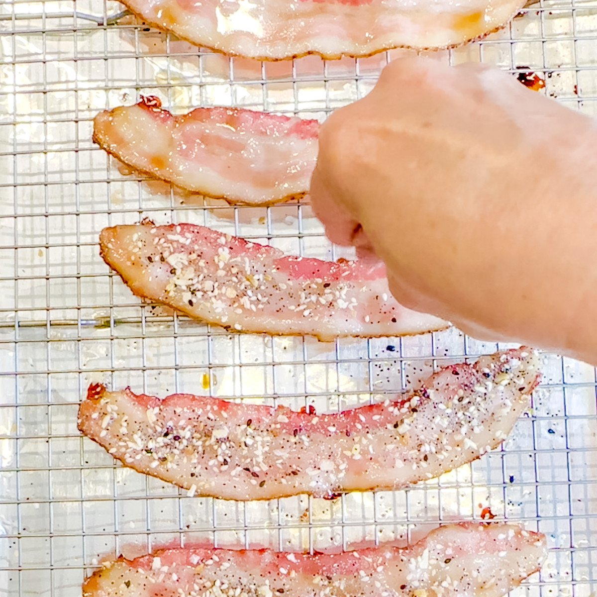 Sprinkling everything seasoning on top of bacon.