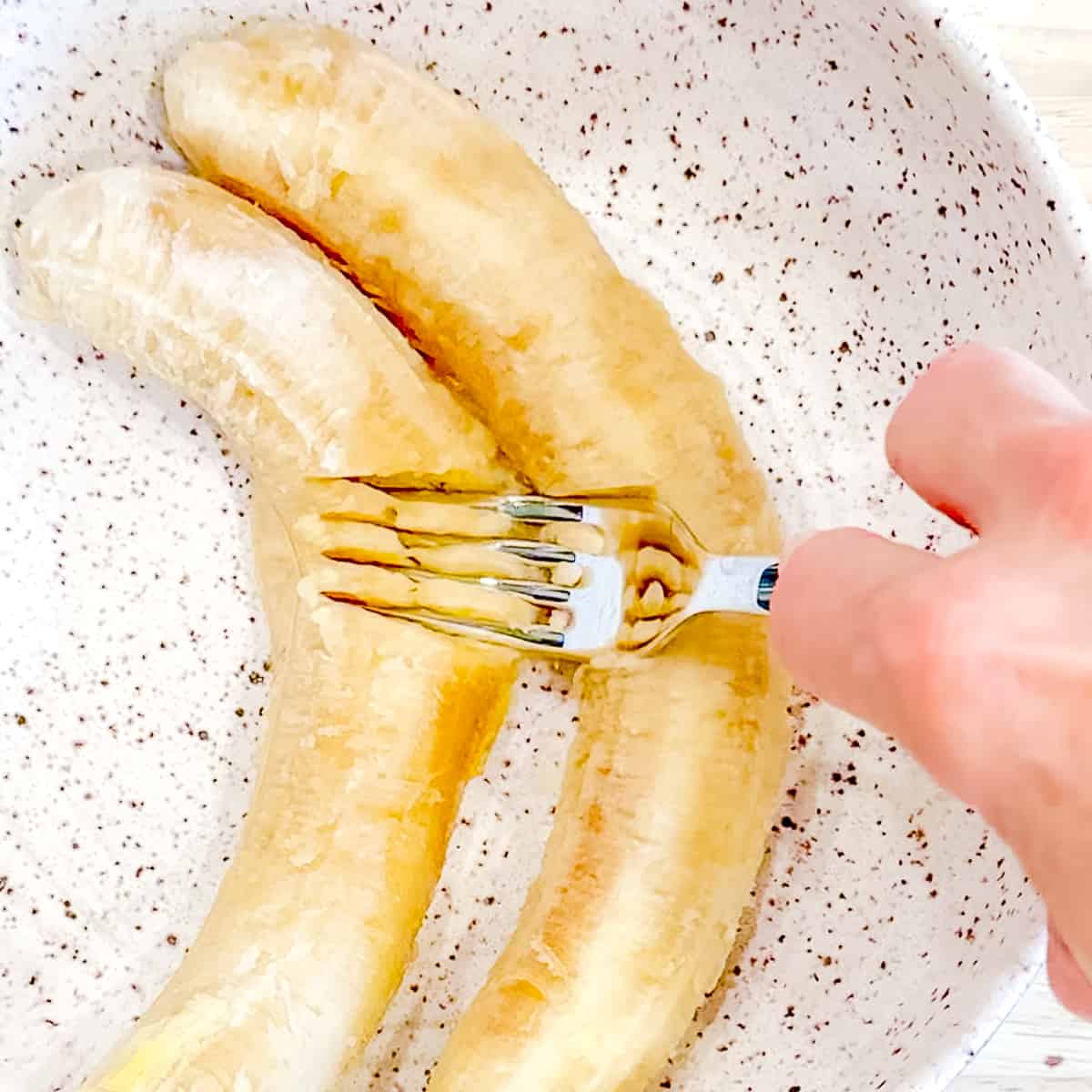 Mashing two bananas with a fork.