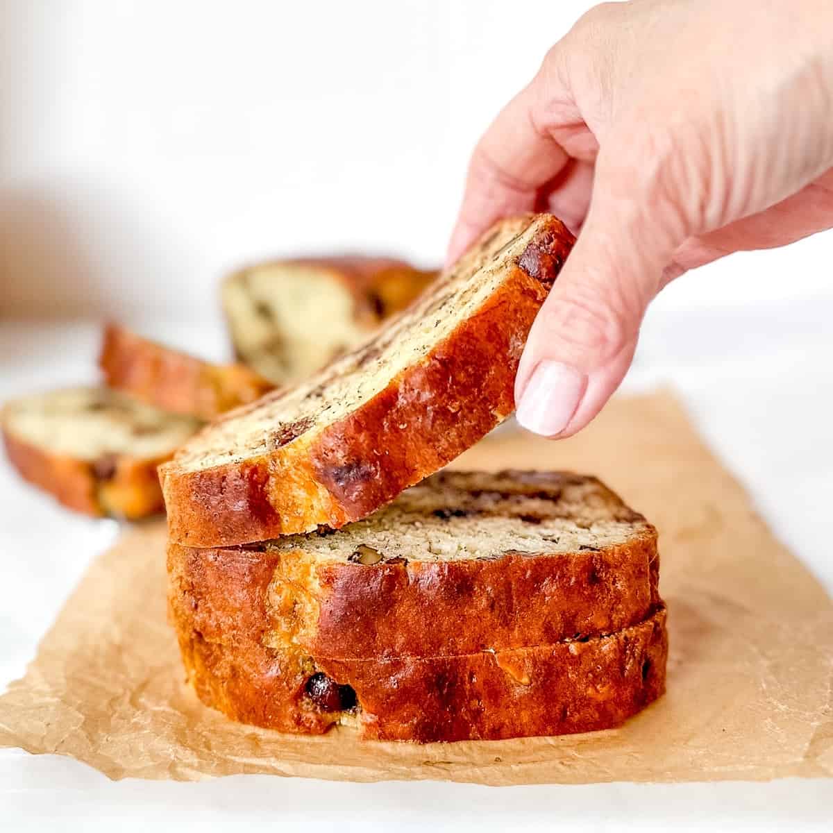 Hand lifting a slice from a stack of banana bread slices.