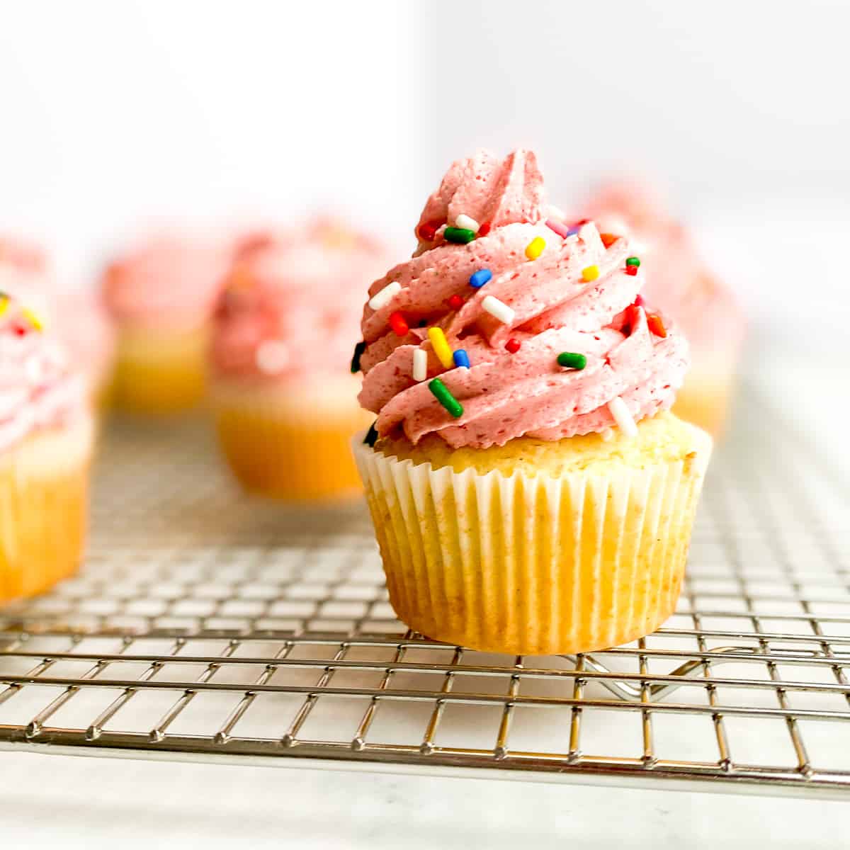 Vanilla cupcakes with strawberry frosting on a wire rack.