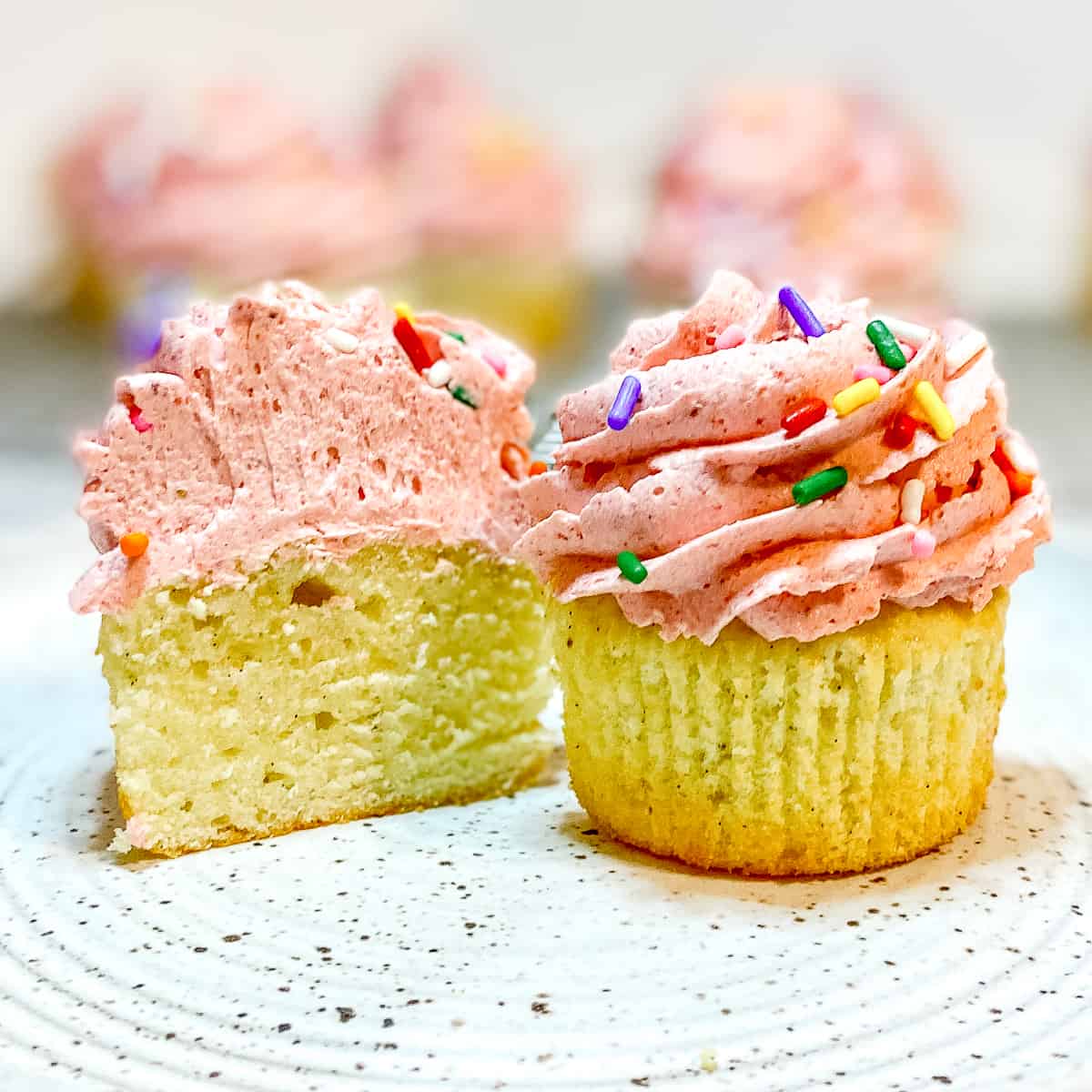 Vanilla cupcakes with strawberry frosting on a white plate.