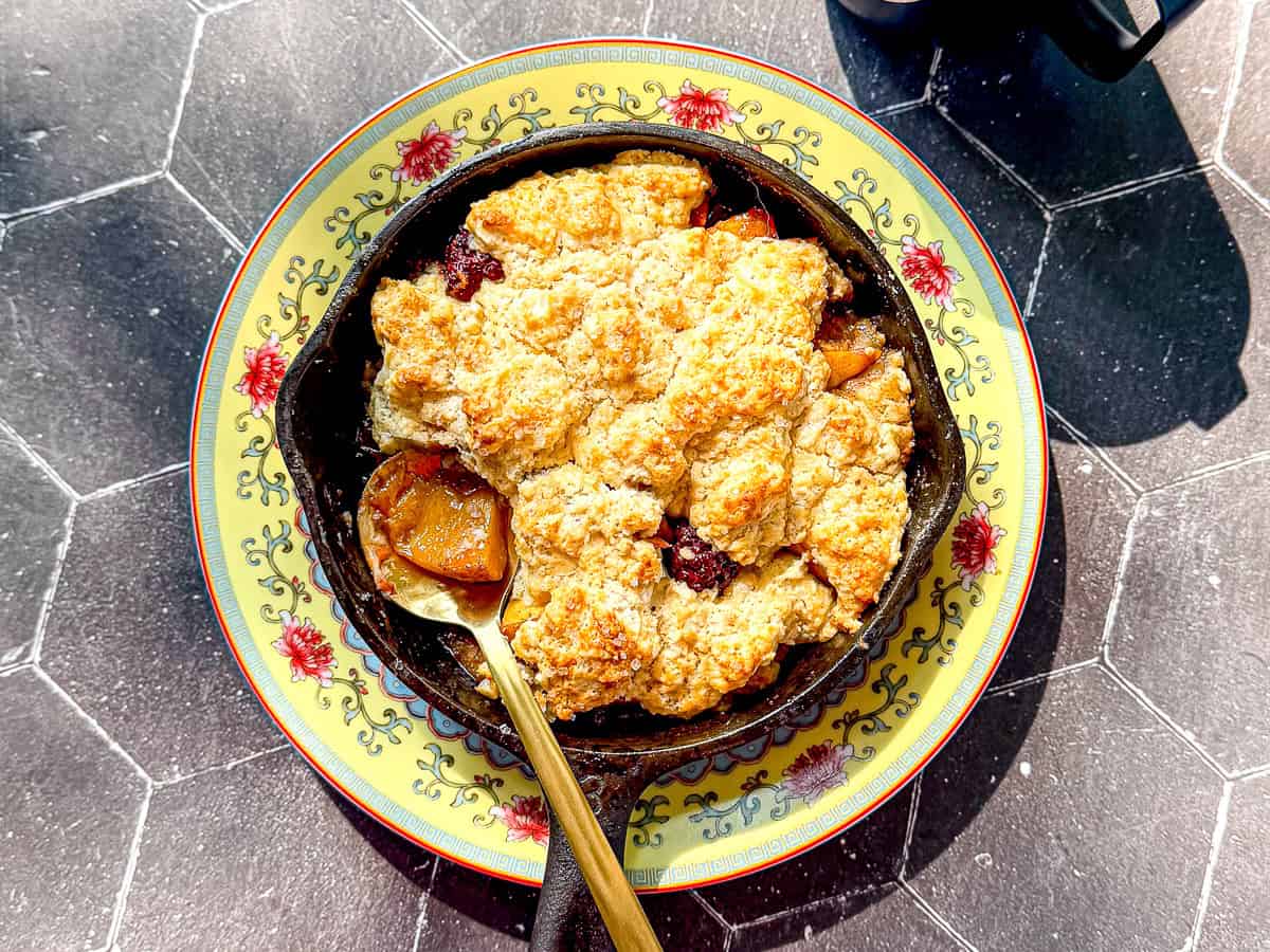 An individual blackberry peach cobbler in a small cast-iron pan on a yellow floral plate.
