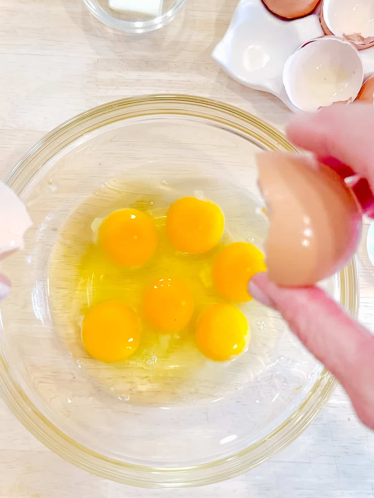 Cracking six eggs into a glass bowl.