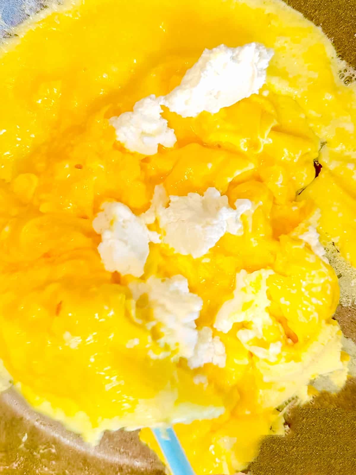 Folding scrambled eggs over ricotta cheese.