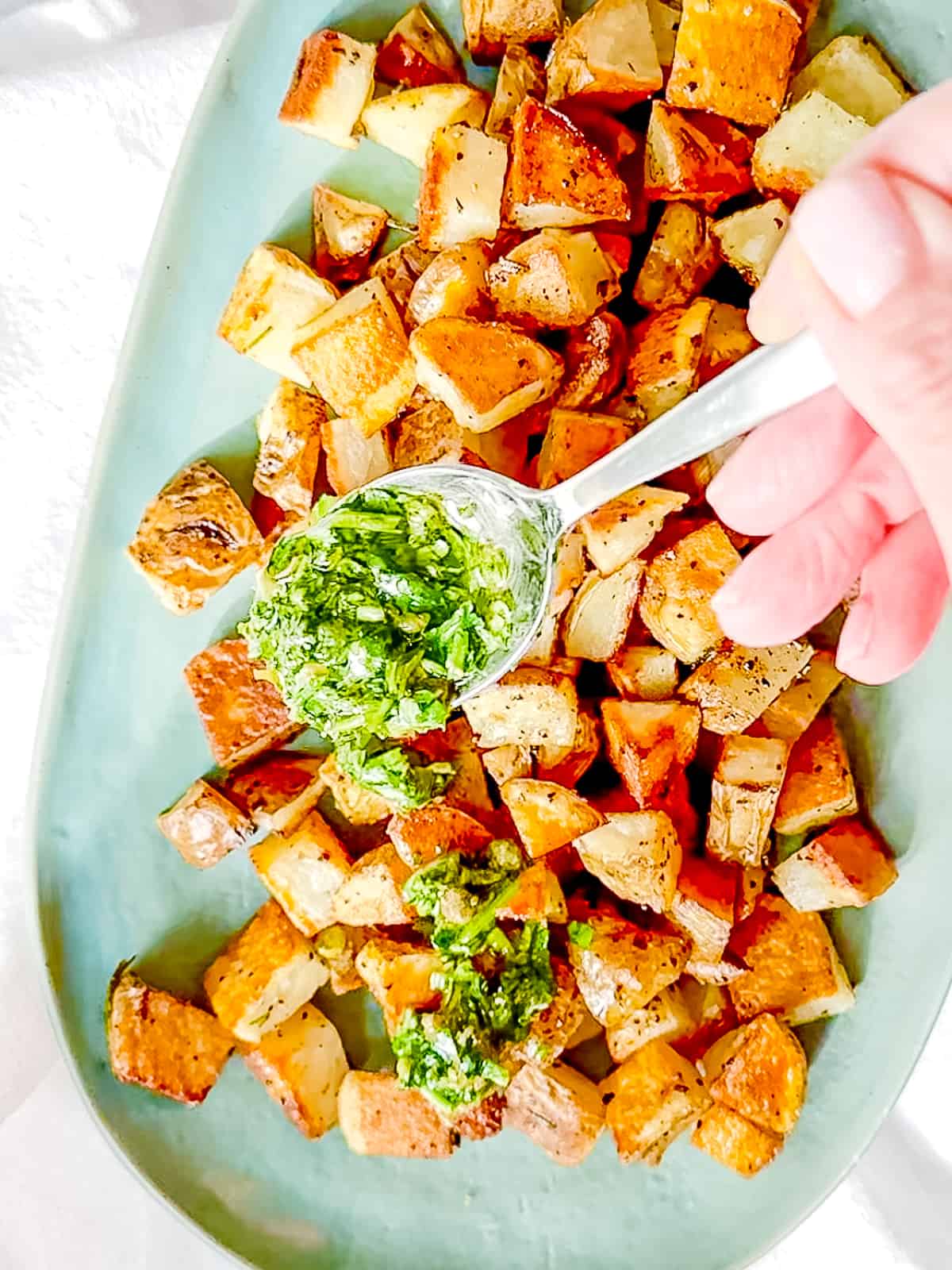 Spooning salsa verde on top of crispy roasted potatoes.