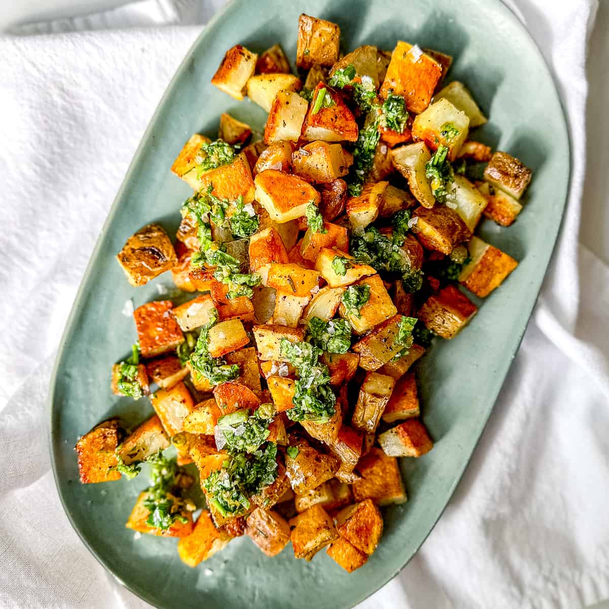 Crispy roasted potatoes with salsa verde on a green platter.