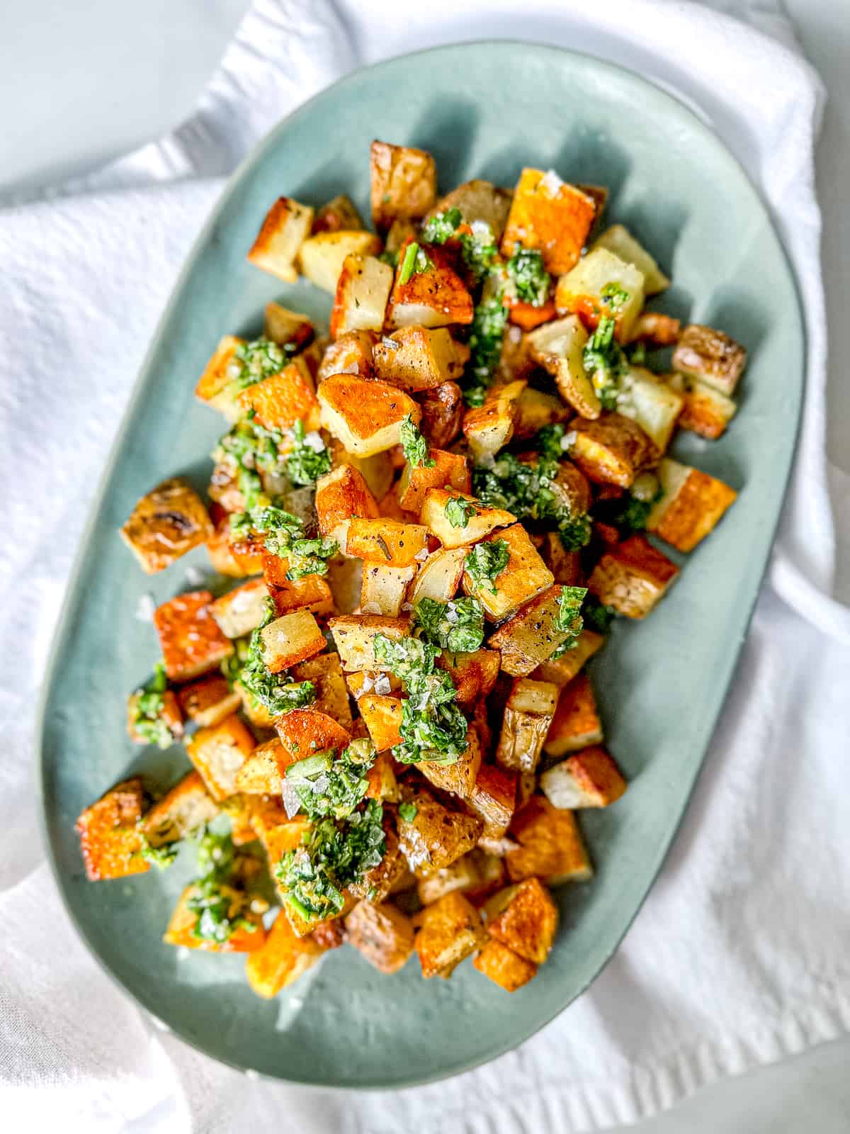 Crispy roasted potatoes with salsa verde on a green platter.