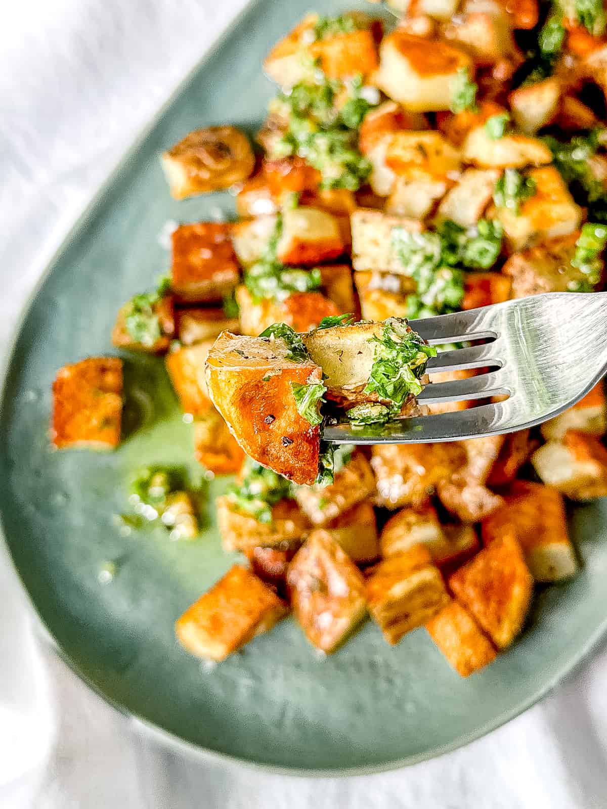 A fork holding two pieces of crispy roasted potatoes with salsa verde.