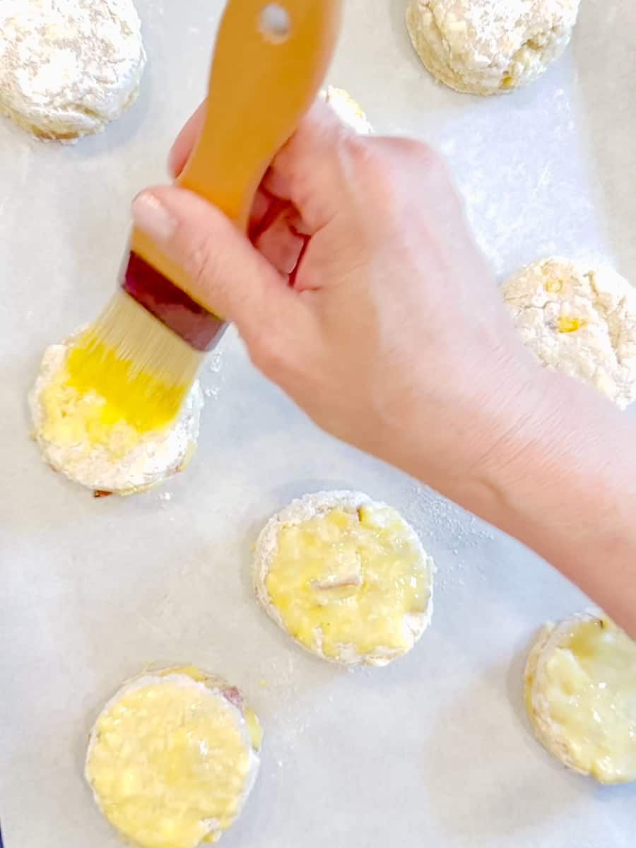 Brushing egg wash on top of peach streusel biscuits.