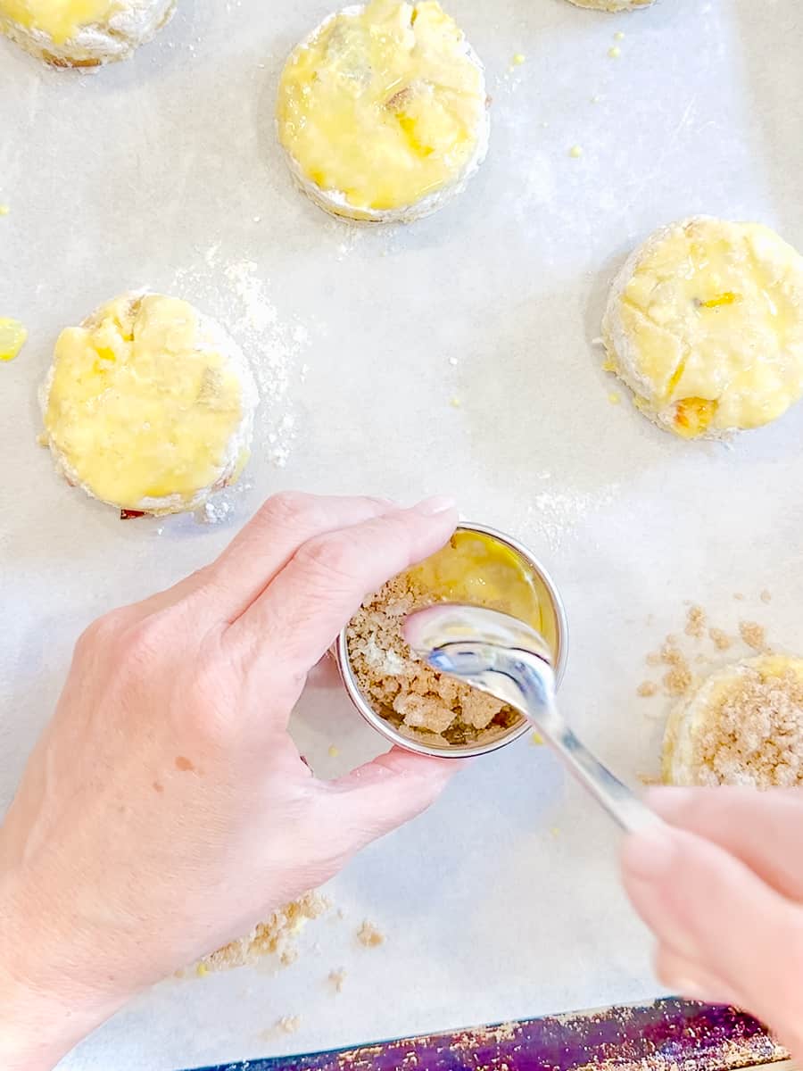 Adding streusel to the tops of unbaked peach biscuits.