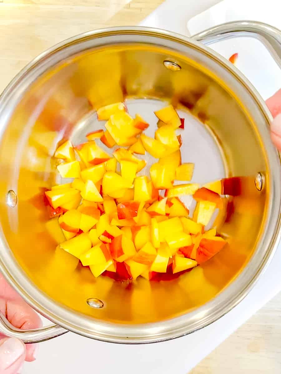 Adding diced peaches to a saucepan with 2 tablespoons of water.