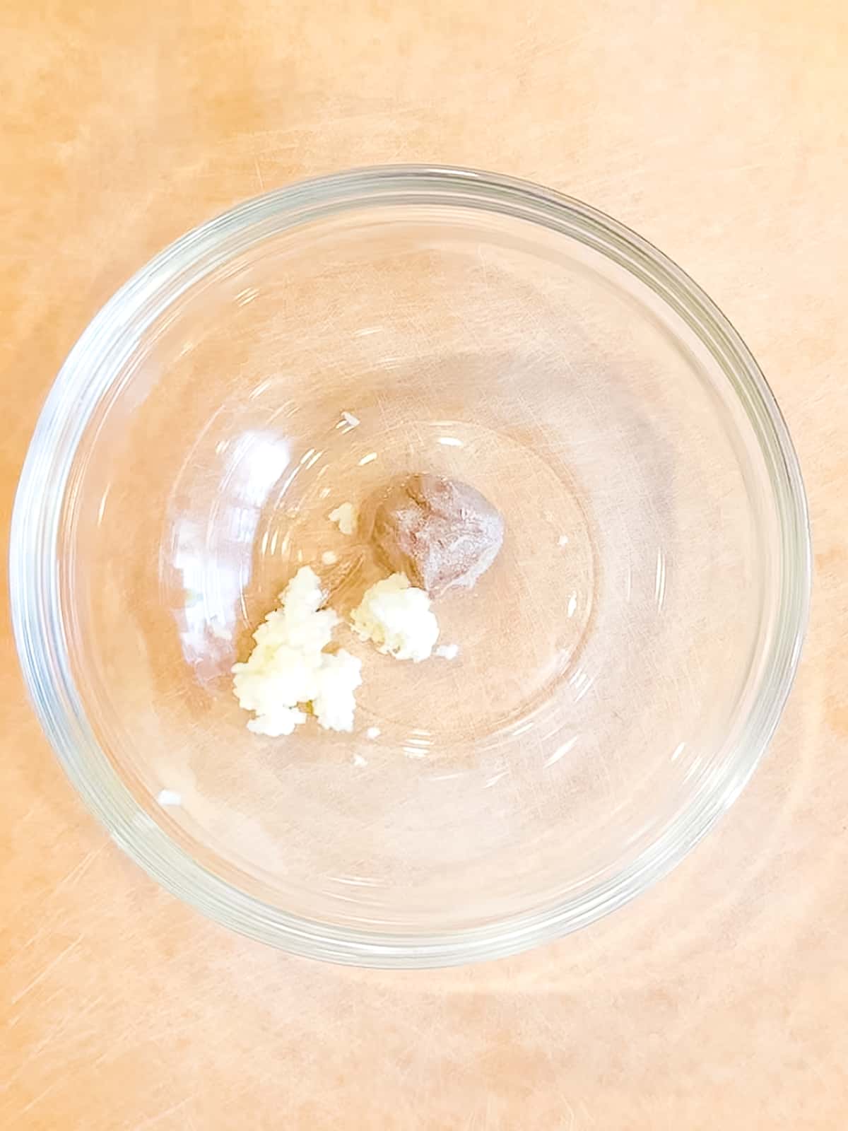 Anchovy paste and grated garlic in a glass bowl.