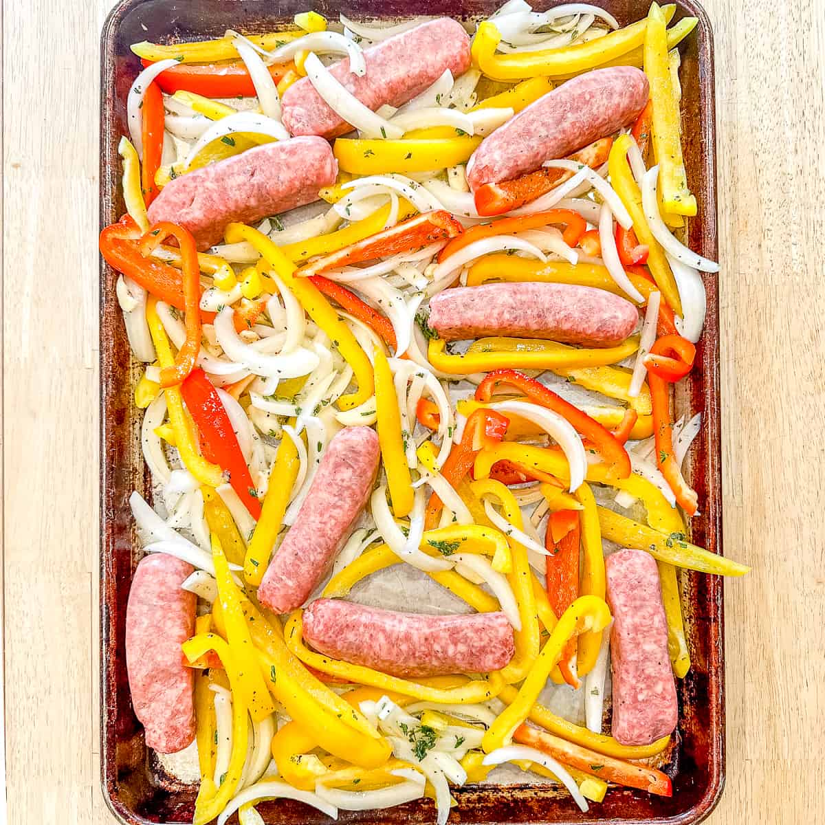 Sheet pan containing uncooked sausage and peppers.