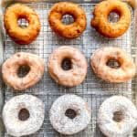 Plain, glazed, and powdered sugar donuts on a wire rack.