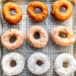 Plain, glazed, and powdered sugar donuts on a wire rack.