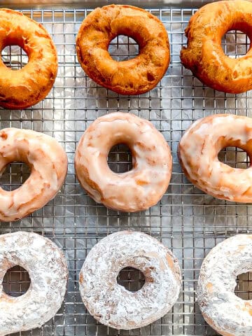 Plain, glazed, and powdered sugar donuts on a wire rack.