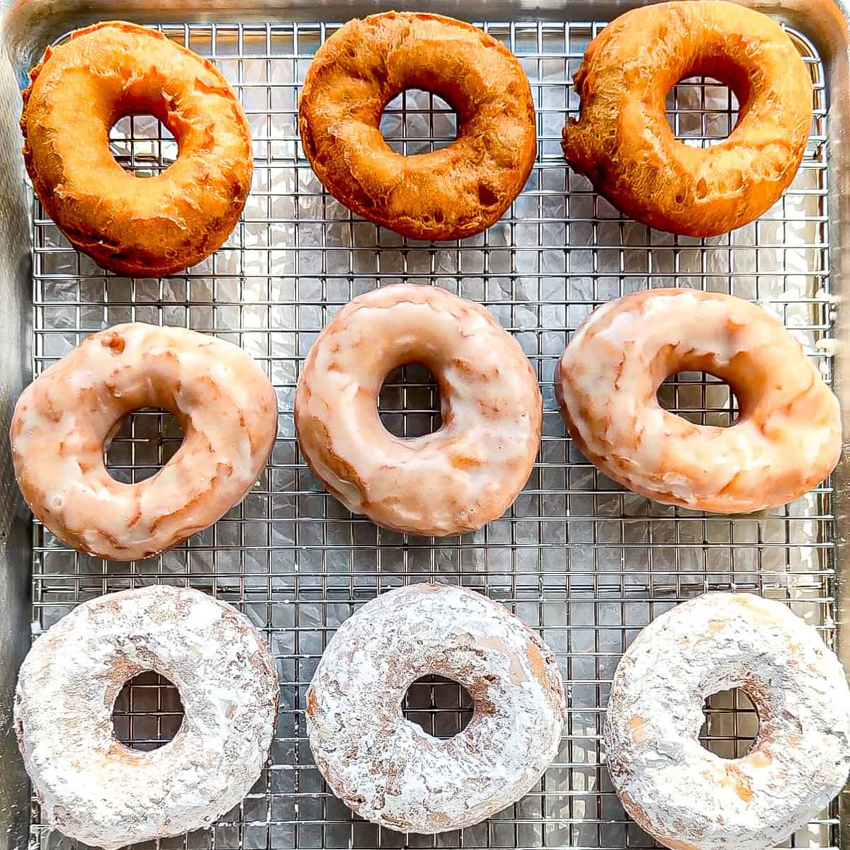 Plain, glazed, and powdered sugar donuts on a wire rack.