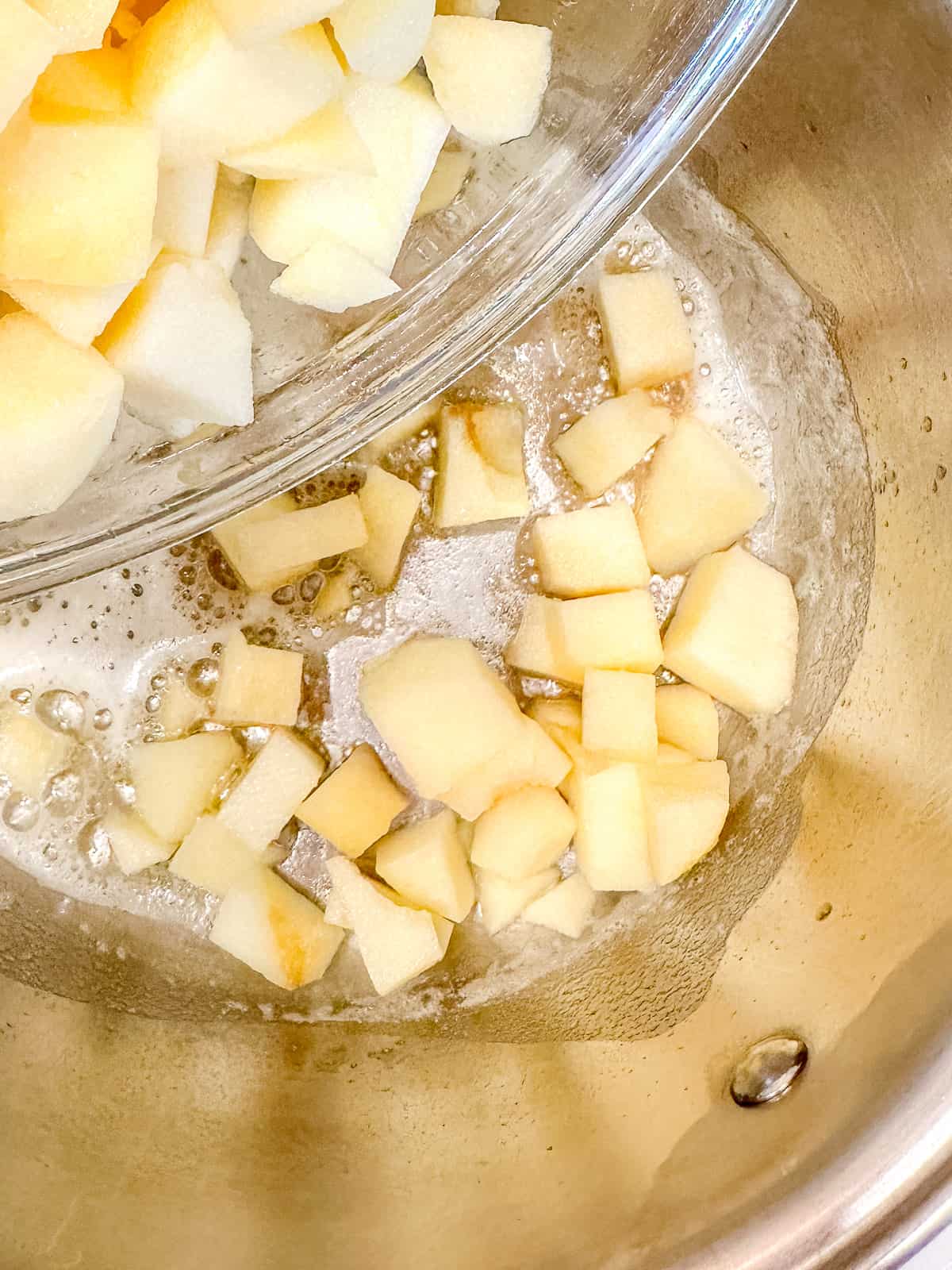 Adding apples to brown butter in a pot.
