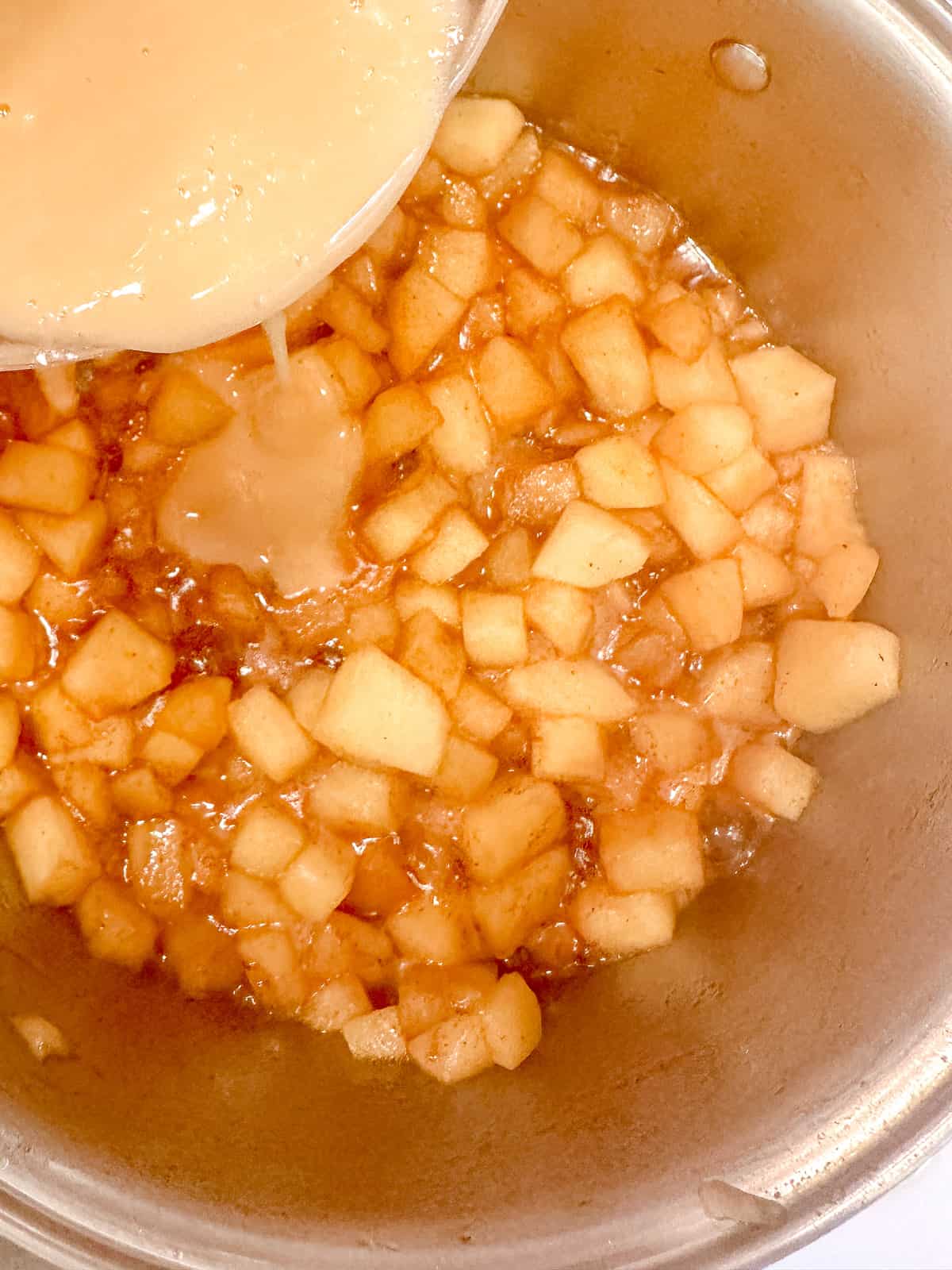 Drizzling a slurry of cornstarch and maple syrup into cooked apples.