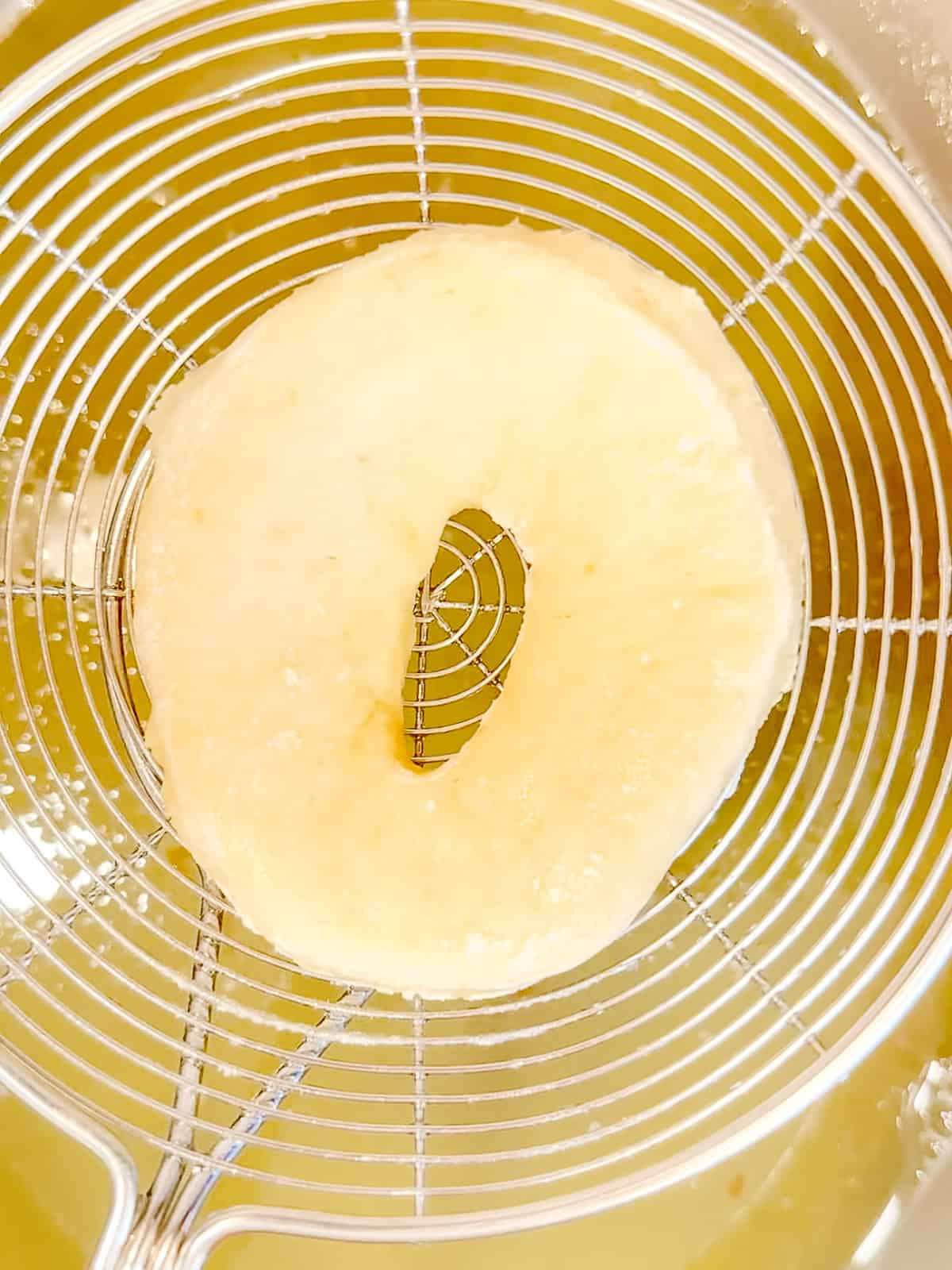 Lowering a donut into hot oil.