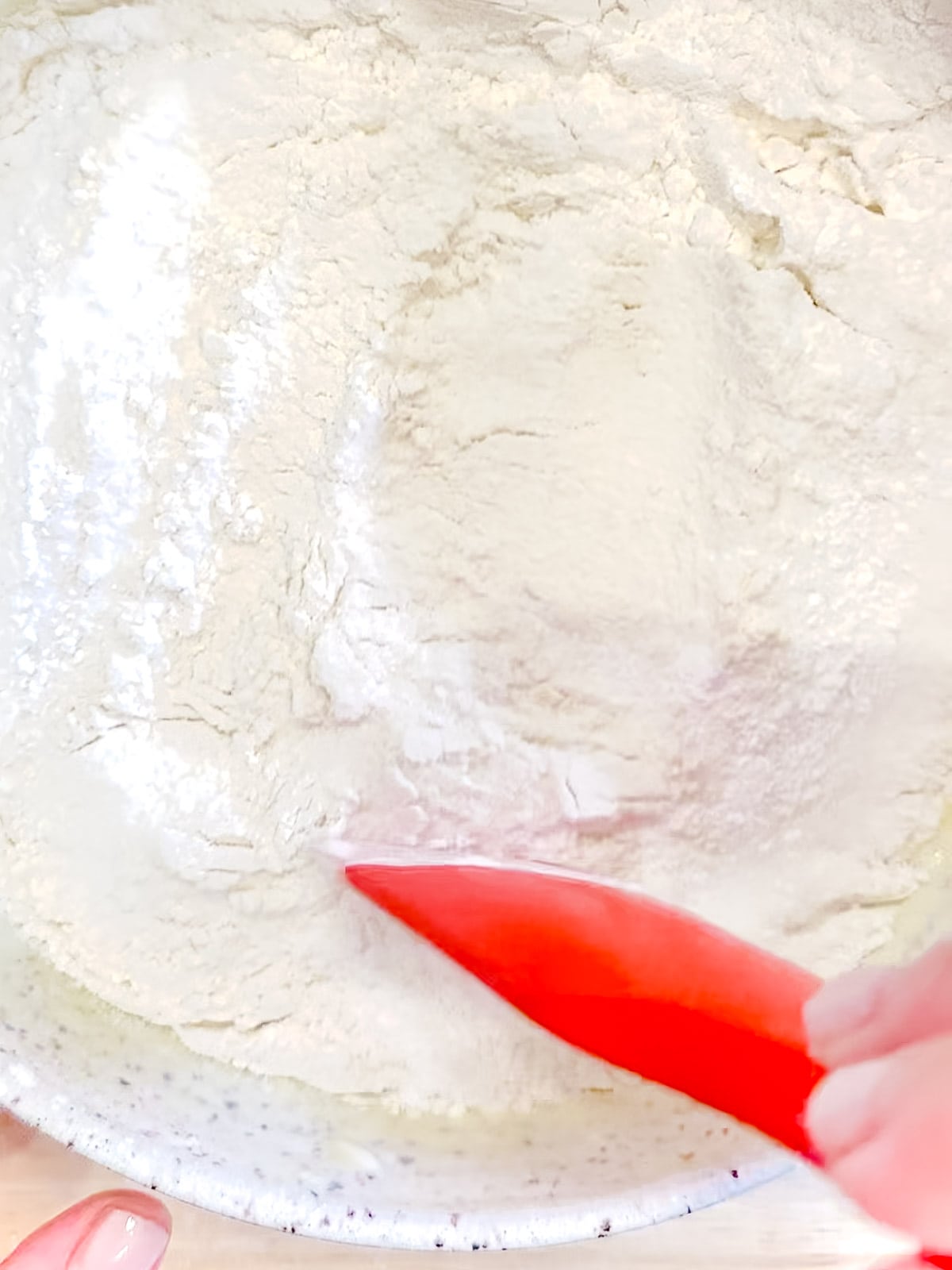 Using a silicone spatula to lightly mix dry ingredients on top of the wet ingredients.