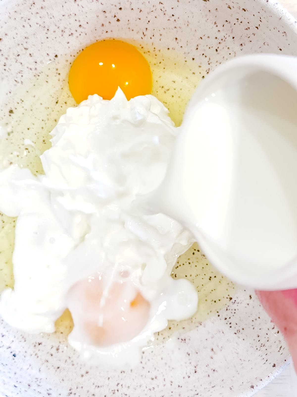 Adding milk to yogurt pancake wet ingredients.