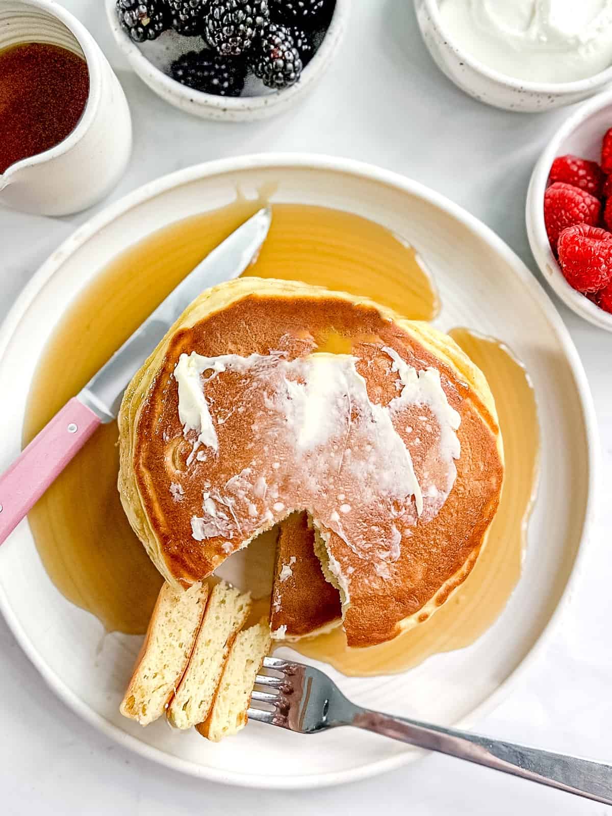 A plate of greek yogurt pancakes with fruit and syrup.