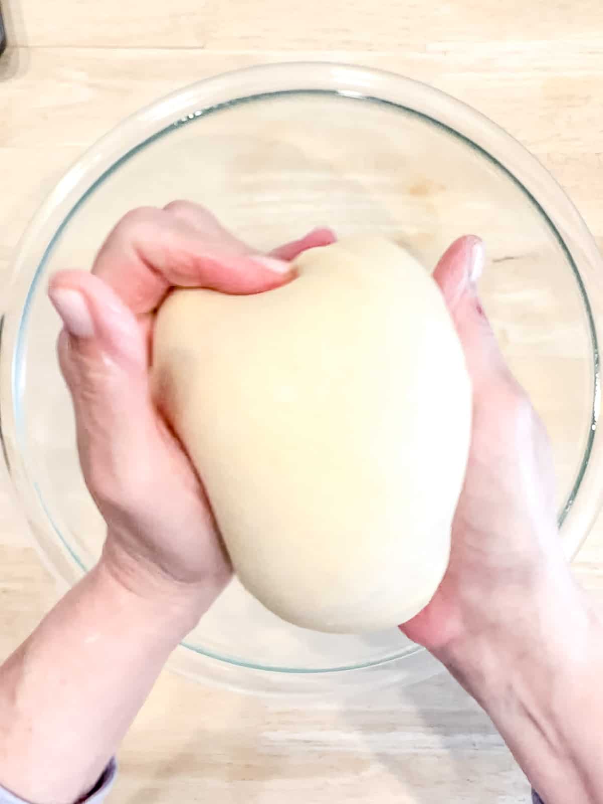 Stretching the top of dough to form a taut ball.