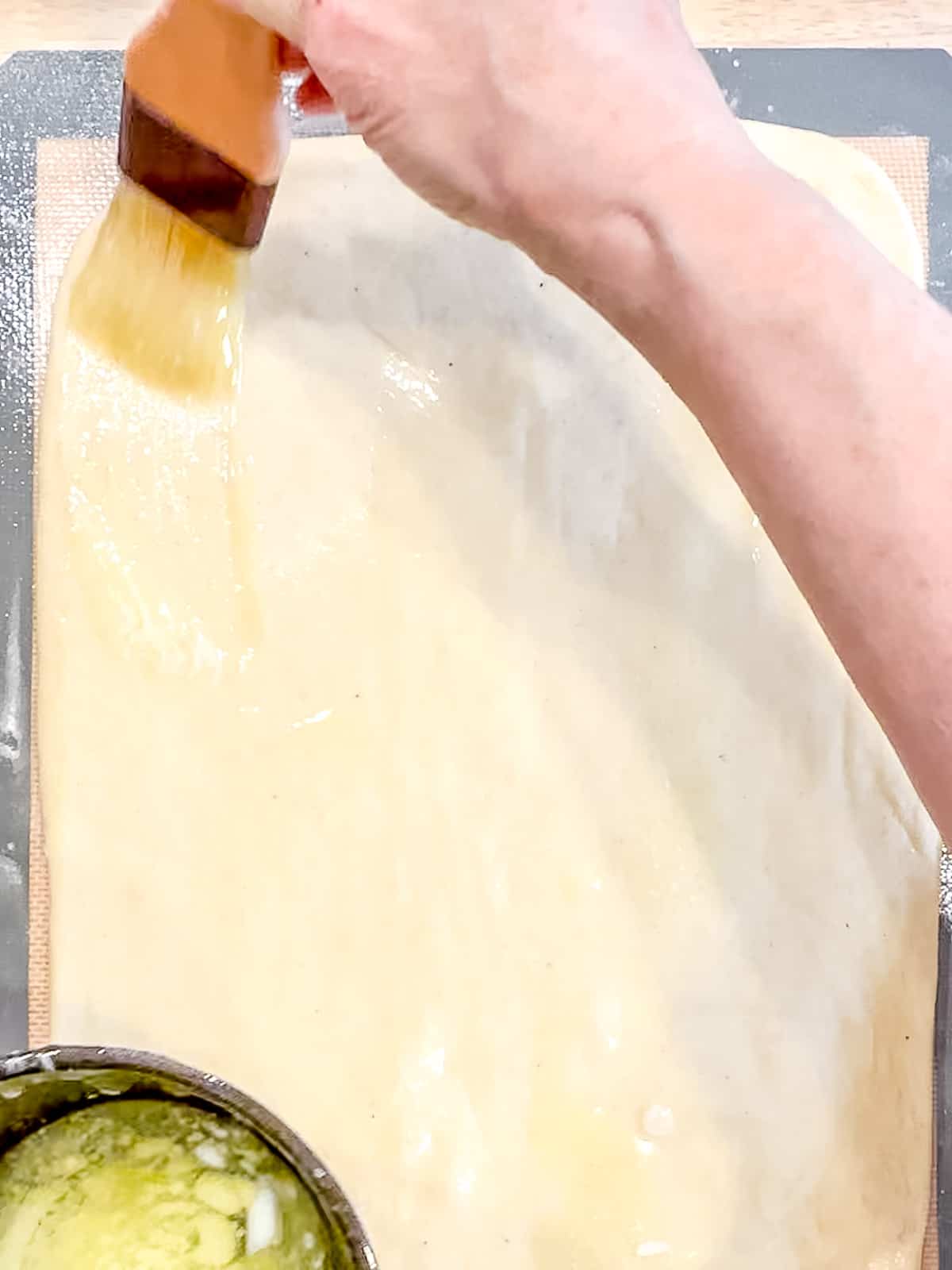 Brushing butter on a rolled out piece of dough.