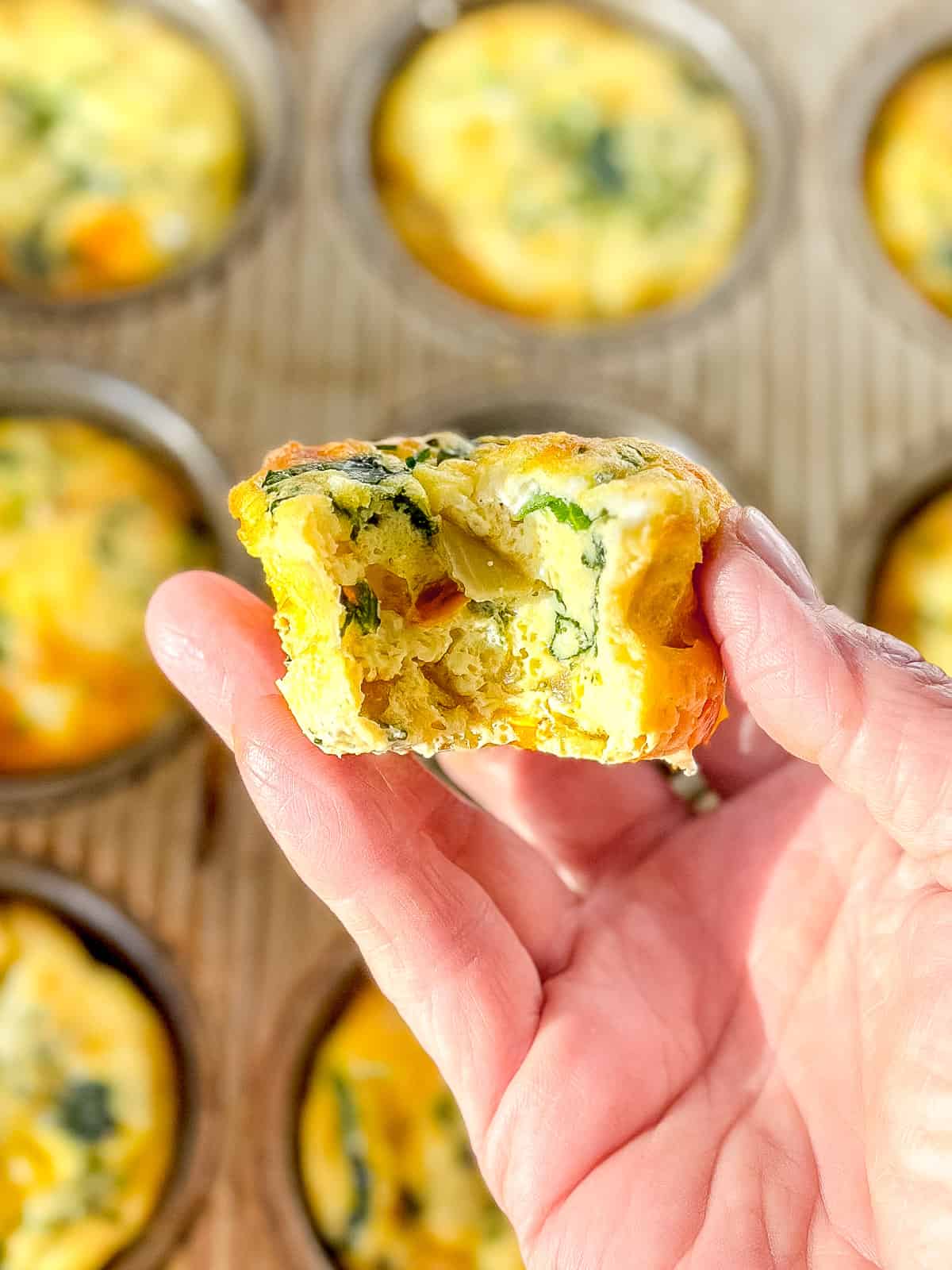 Holding a muffin pan frittata with a bite taken out.