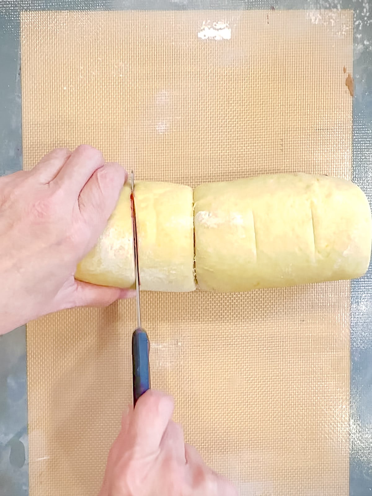 Using a serrated knife to cut blueberry, orange, cinnamon rolls.