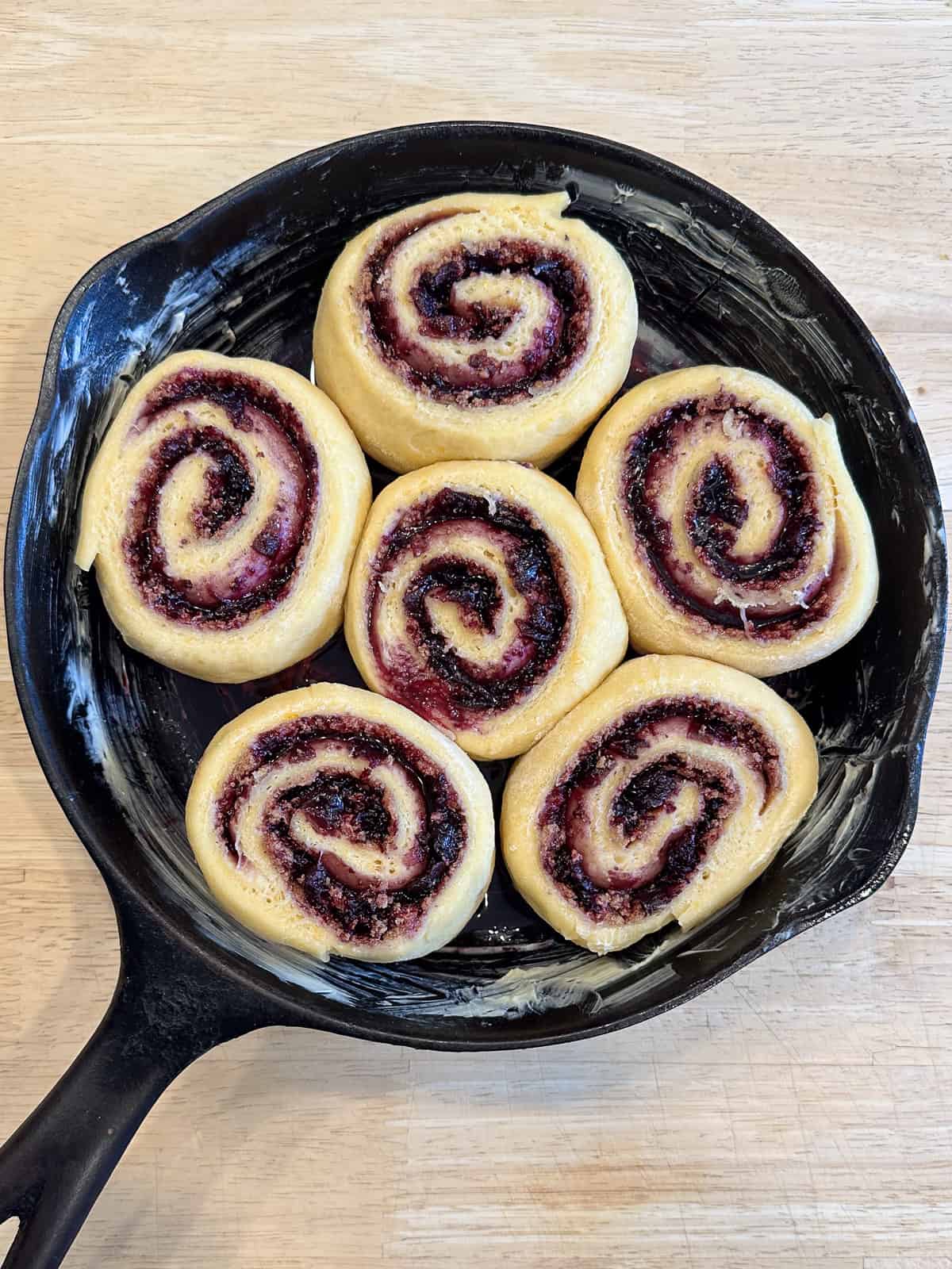 A cast iron pan filled with blueberry orange cinnamon rolls that have risen overnight.