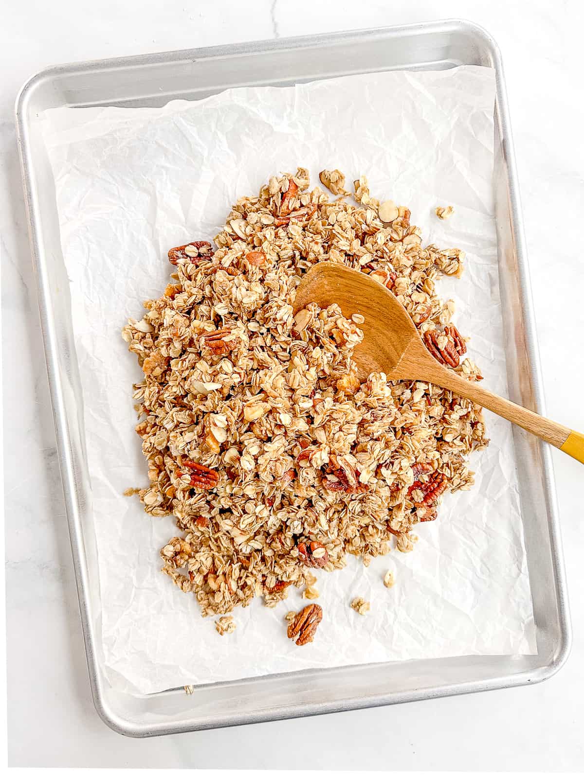 Spreading unbaked granola on a parchment paper lined sheet pan.