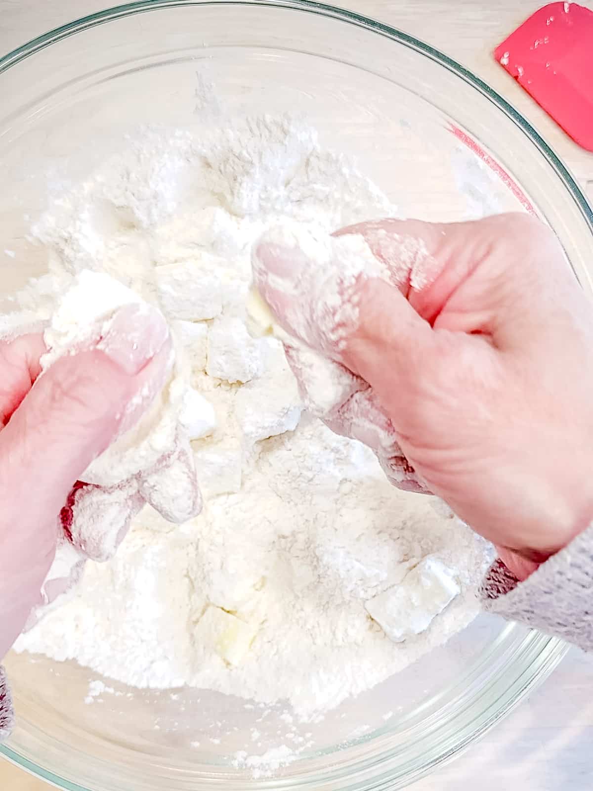 Rubbing butter and cream cheese into flour with fingers for biscuits.