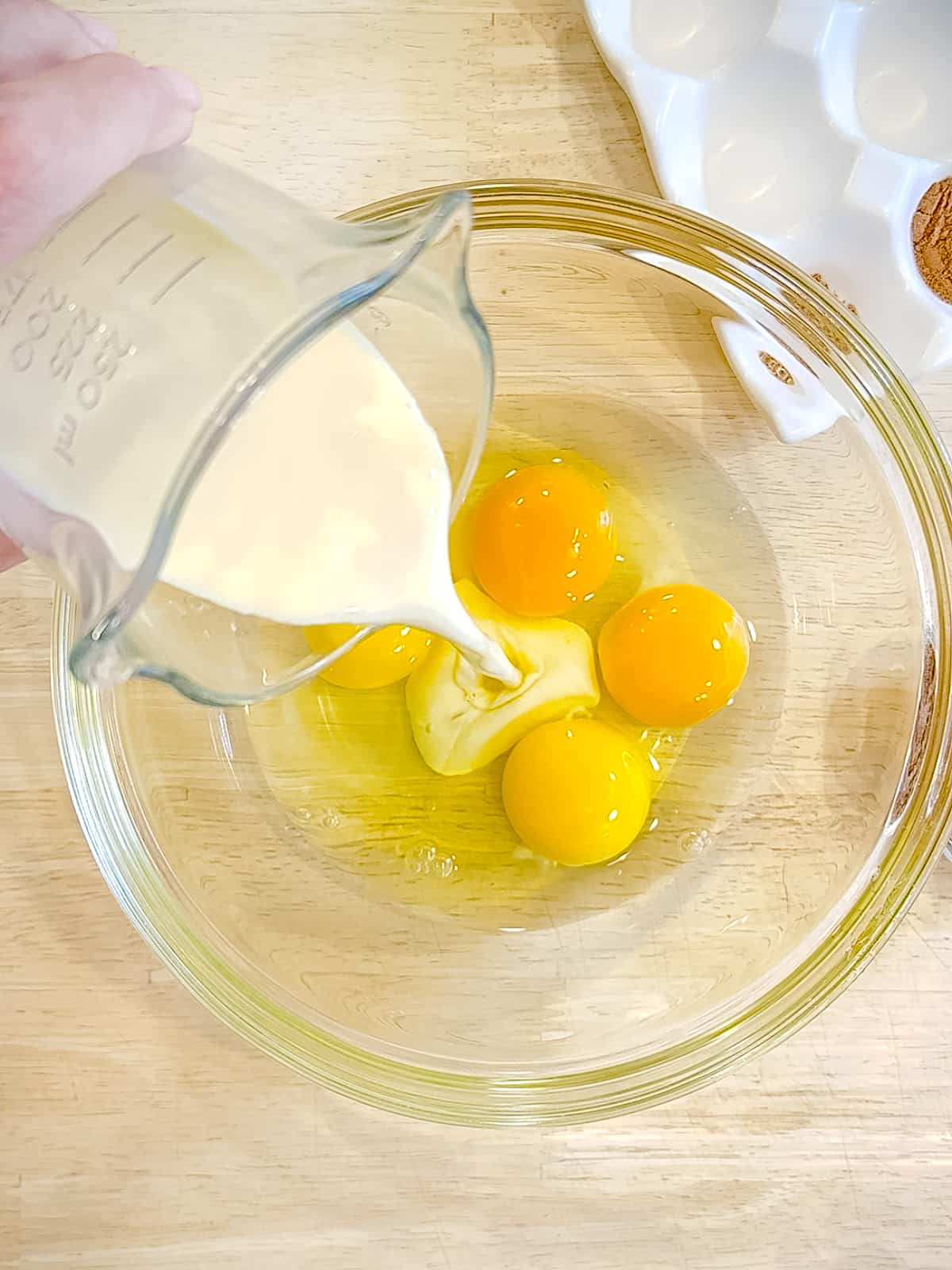 Pouring eggnog into bowl with four eggs.